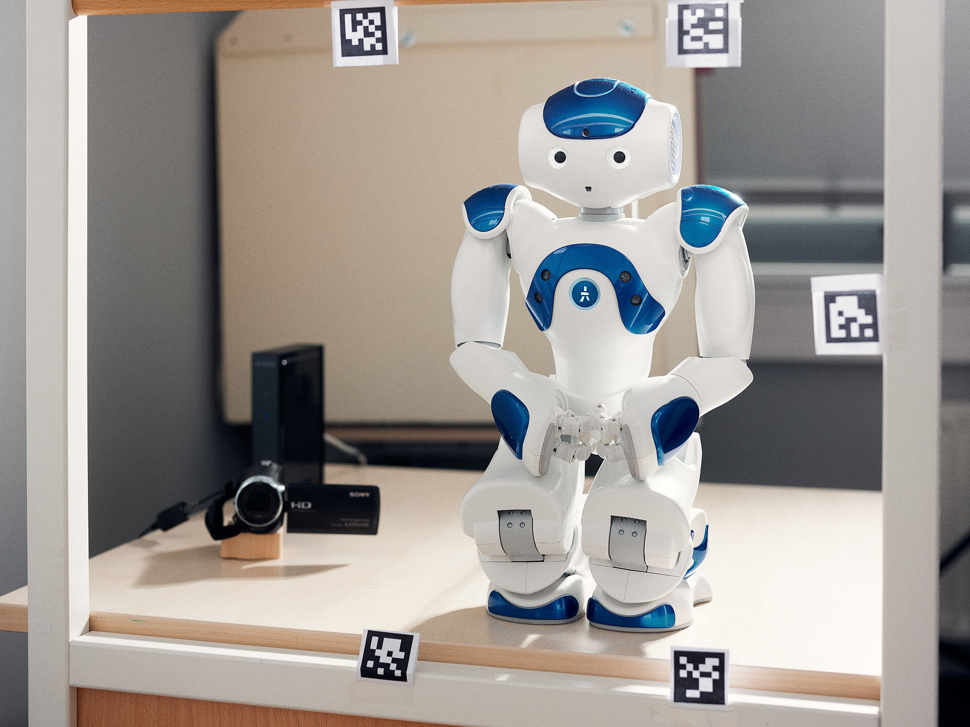 Ein KI-Roboter steht hinter einer Glasscheibe, die mit QR-Codes beklebt ist.