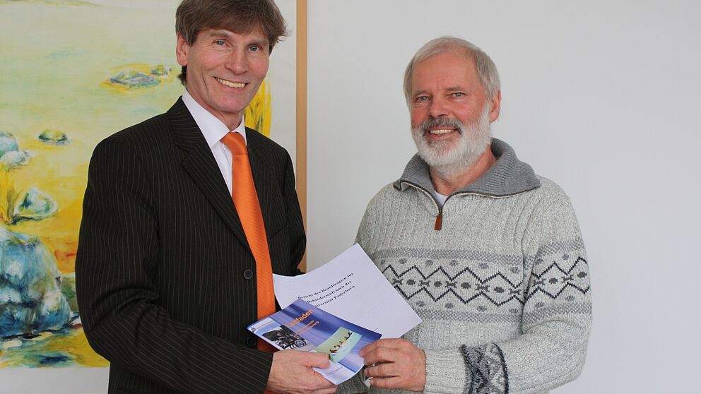 Foto (Universität Paderborn, Frauke Döll): Dr. Uwe Rheker (rechts) übergibt seinen letzten Bericht als Beauftragter für Behindertenfragen der Universität an Präsident Prof. Dr. Nikolaus Risch.