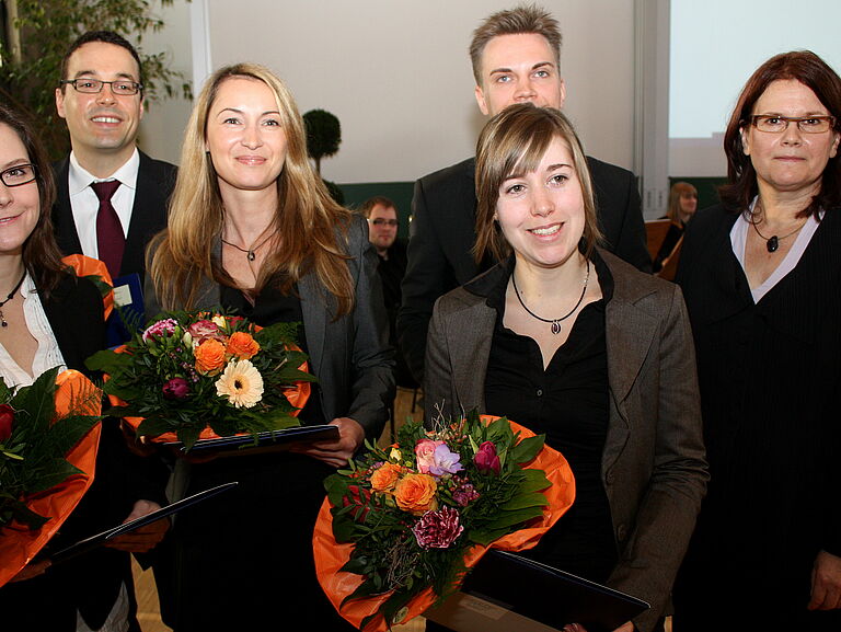 Die fünf Lehrpreisträger:innen stehen neben der Vizepräsidentin vorne im Hörsaal und halten Blumensträuße in der Hand. 