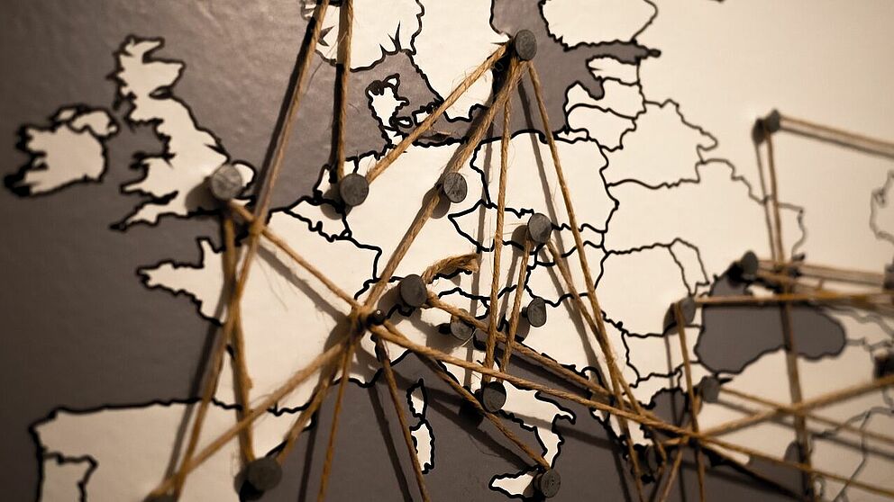 Symbolbild: Europakarte mit Pinnadeln, die mit Fäden miteinander verbunden sind.