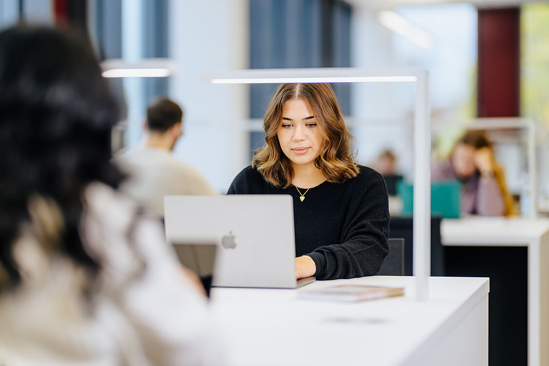 Student sits in front of a table and types on a notebook.