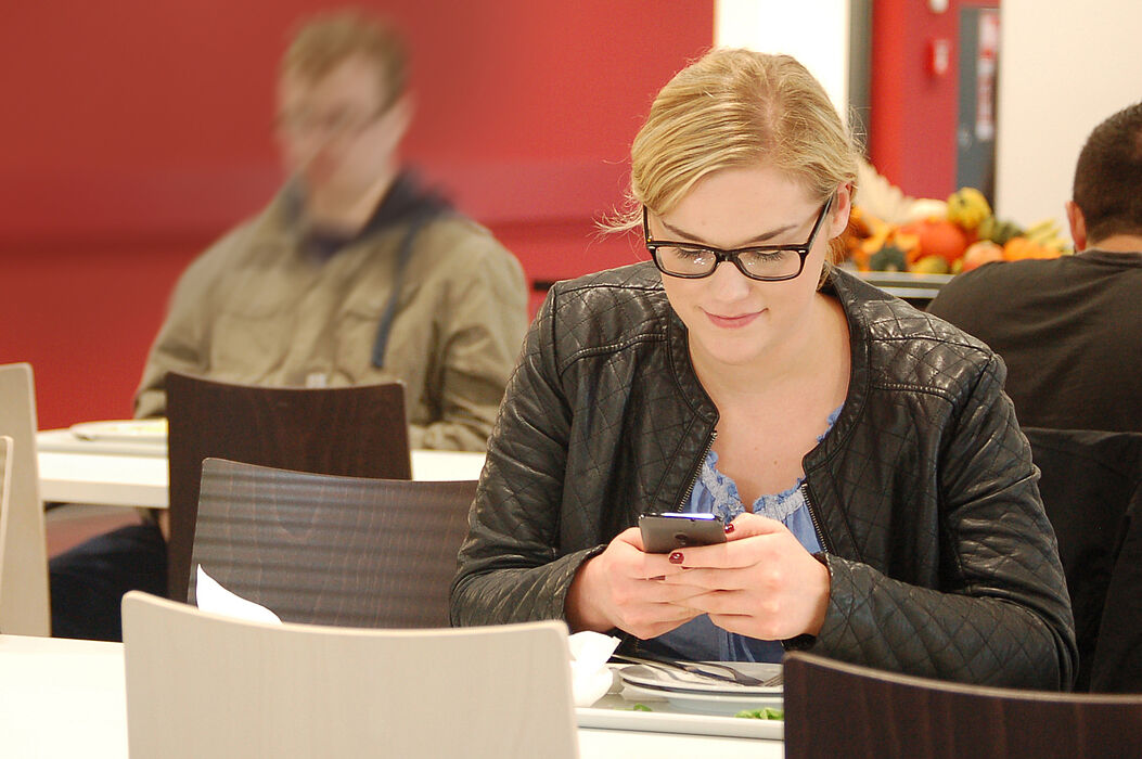 Foto (Studierendenwerk Paderborn): Studentin in der Mensa Forum des Studierendenwerks Paderborn auf dem Campus der Universität Paderborn – Mobiler Informationsabruf.