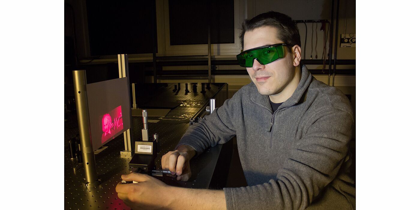 Foto (Universität Paderborn): Doktorand Holger Mühlenbernd demonstriert im Optiklabor die Erzeugung einer holografischen Abbildung.