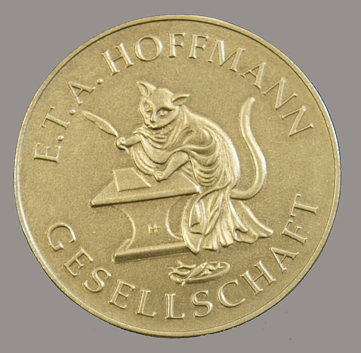 Die Medaille zeigt einen Romanhelden E.T.A. Hoffmanns, den schreibenden Kater Murr, und auf der Rückseite das Profil Hoffmanns.