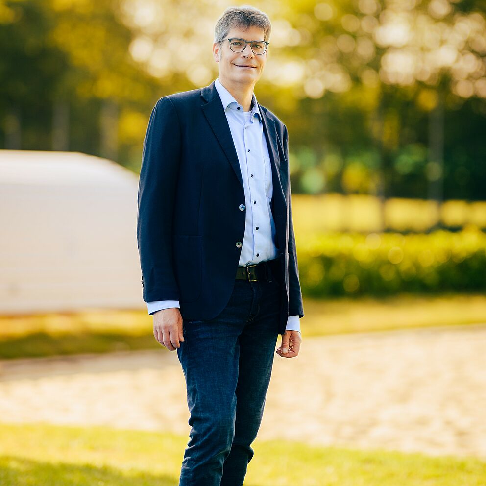 Der Vizepräsident für Wissens- und Technologietransfer der Universität Paderborn René Fahr steht vor einem unscharfen Bäumen im Hintergrund.