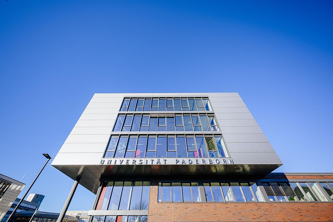 Das Q-Gebäude der Universität Paderborn erstreckt sich vor blauem Himmel mit seiner modernen Fensterfront in die Höhe.