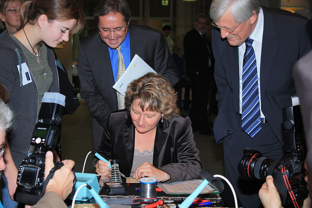 Foto (Referat Presse und Kommunikation, Universität Paderborn, Frauke Döll): Umgeben von Blitzlichtgewitter verlötet Ministerin Schulze den Schaltplan für einen Digitalen Würfel, den die Jahrgangsstufe 10 der Friedrich-von-Spee-Gesamtschule vorstellt
