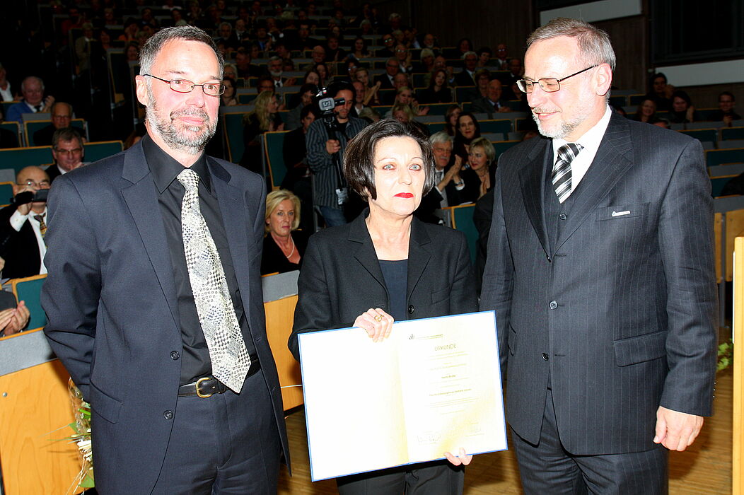 Foto (Universität Paderborn, Patrick Kleibold): Verleihung der Ehrendoktorwürde an die Literatur-Nobelpreisträgerin Herta Müller: Prof. Dr. Norbert Otto Eke (links) und Prof. Dr. Volker Peckhaus überreichen die Ehrenpromotion an Herta Müller.