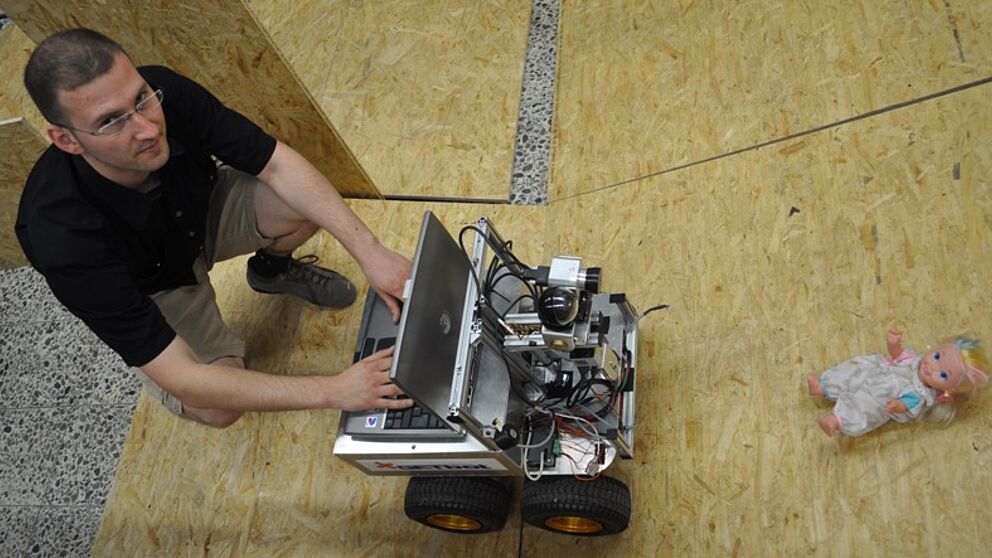 Foto (Mark Heinemann): Rettungsroboter: Dipl.-Inform. Tobias Kotthäuser von der Universität Paderborn demonstriert ein aktuelles Forschungsprojekt aus dem „GET Lab“. Mit Hilfe von Sensoren sucht ein Rettungsroboter in einer Arena, die meist einem Ka