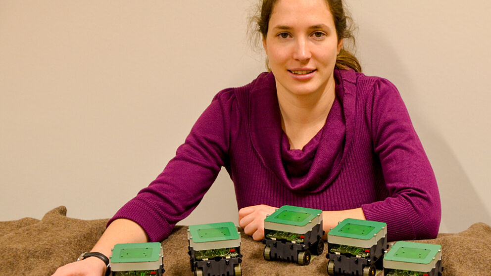 Foto (Universität Paderborn, Jana Neuhaus): Autonome Roboter formieren sich in unbekanntem Gelände zu einer Linie – Dr. Barbara Kempkes vor einem Modellaufbau.