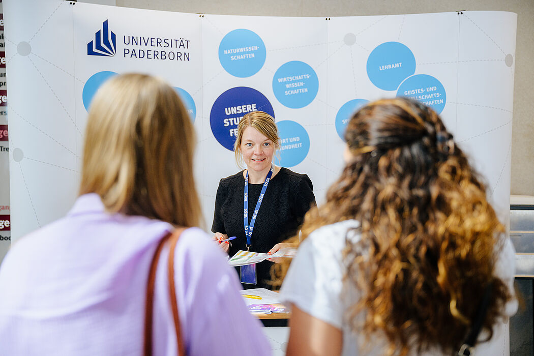 Zwei Schülerinnen informieren sich bei einer Universitätsmitarbeiterin über Studienmöglichkeiten an der Universität Paderborn.