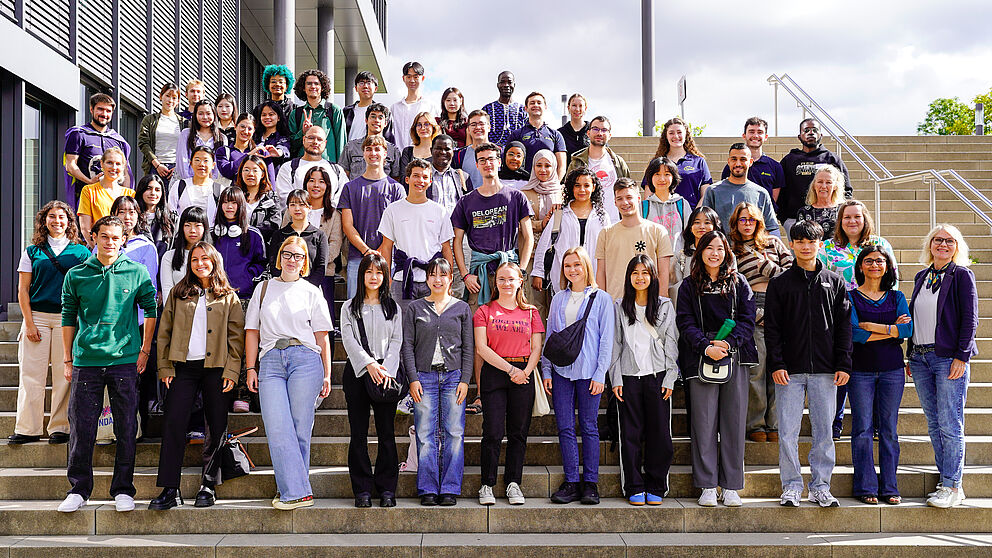 Mehr als 100 Personen stehen als Gruppe auf einer Treppe und lächeln. 