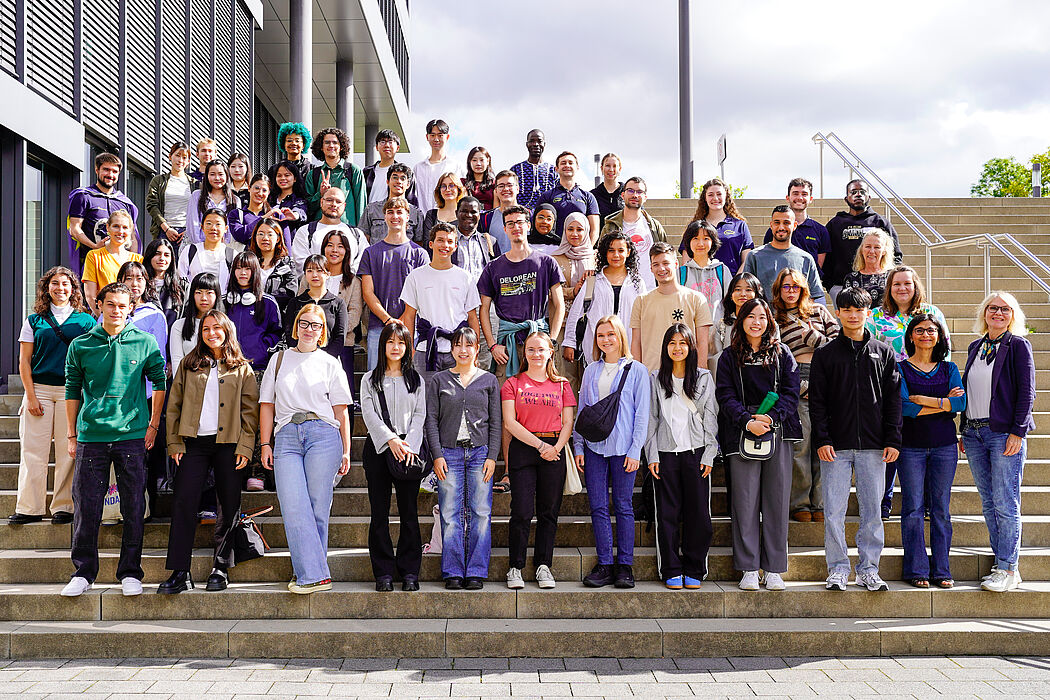 More than 100 people stand as a group on a staircase and smile. 