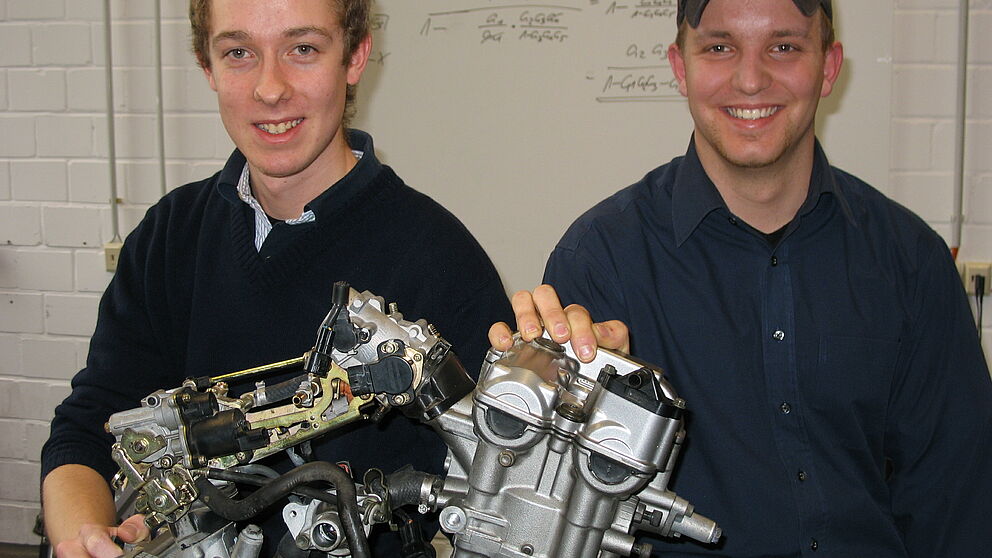 Foto (Christiane Bernert): Lars Heisel (li.) und Nils Gerhart mit dem Motor des Boliden, der in einer Werkstatt auf dem Uni-Campus entsteht. Der Suzuki SV 650-Motor wird später mit Bio-Ethanol angetrieben, das Auto bekommt einen Turbolader und Allrad-Ant