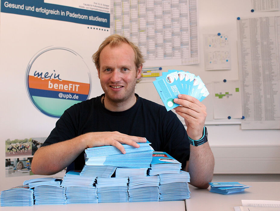 Foto (Universität Paderborn, Heiko Appelbaum): Frisch gedruckt: Dennis Fergland präsentiert die neuen Gesundheitspässe.