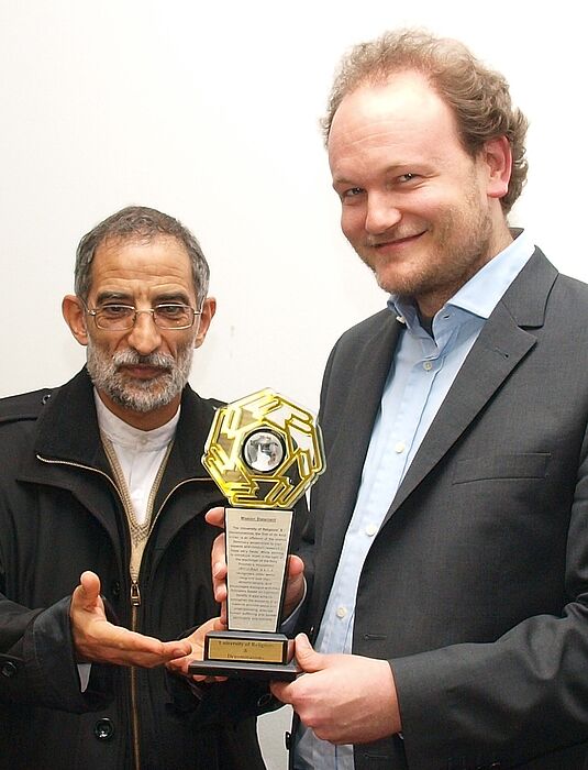 Foto (Universität Paderborn, Martin Decking): Als Zeichen der Anerkennung erhielt Prof. Dr. Klaus von Stosch (r.) von Dr. Mohammad Taghi Ansaripour eine Statue mit dem Logo der iranischen „Universität der Religionen“ überreicht.