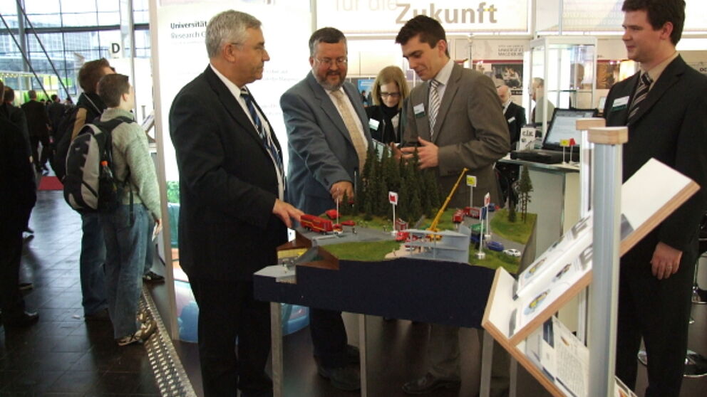 Foto (Lehrstuhl C.I.K): Katastrophenschutz im Miniaturformat: Parl. Staatssekretär Manfred Palmen (Innenministerium NRW) und Staatssekretär Karl Peter Brendel (Innenministerium NRW) mit Dipl.-Ing. Jens Pottebaum und Dipl.-Wirt.-Inf. Benedikt Birkhäuser