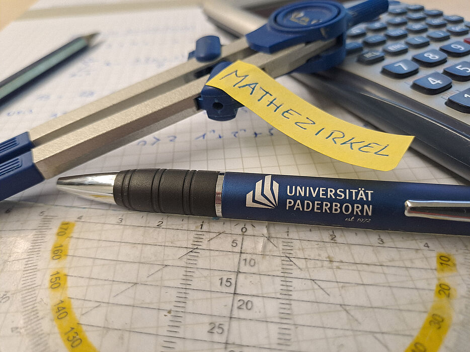 Stift, Taschenrechner, Geodreieck und Zirkel liegen auf Blatt Papier