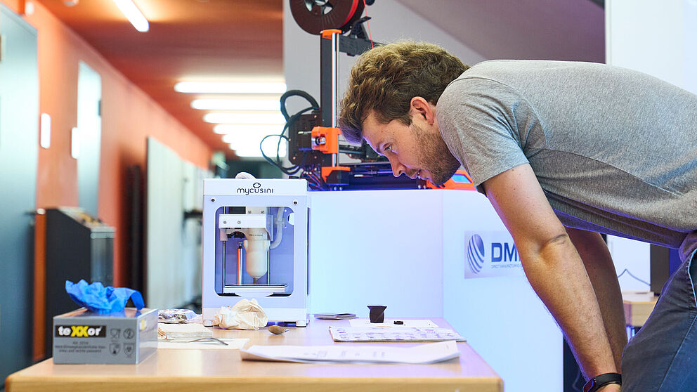 Ein Mann schaut sich verschiedene 3D-Druck-Materialien an, die auf einem Tisch liegen.