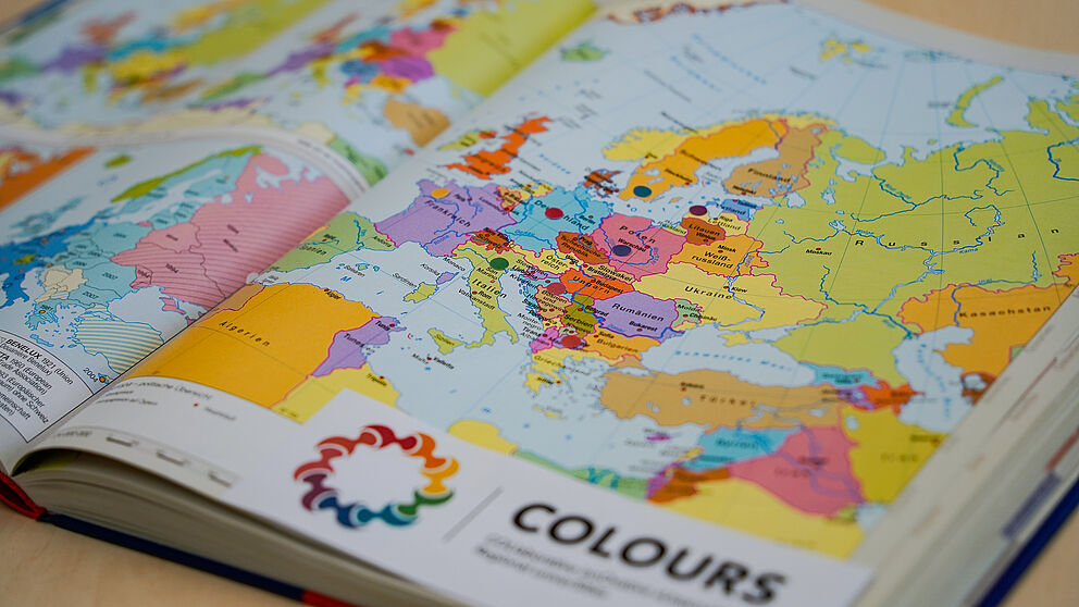Eine Europa-Karte ist mit bunten Punkten beklebt, die symbolisch für die Mitgliedsstaaten der Hochschulallianz "COLOURS" stehen. Das Logo der Allianz ist am Bildrand angeschnitten.