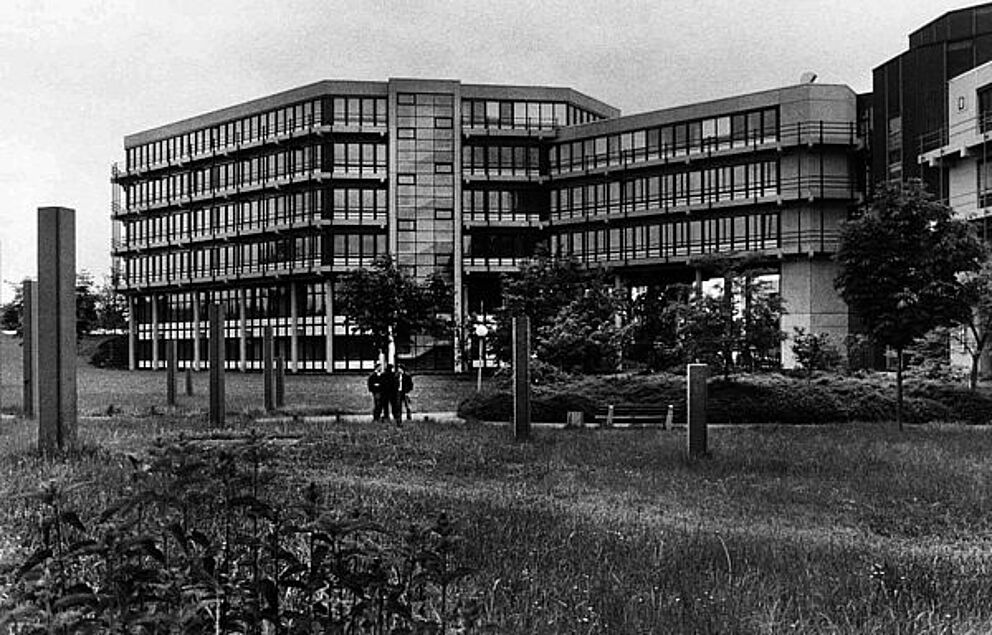 Schwarz-weiß Foto von einem mehrstöckigen Universitätsgebäude, im Vordergrund Wiese.