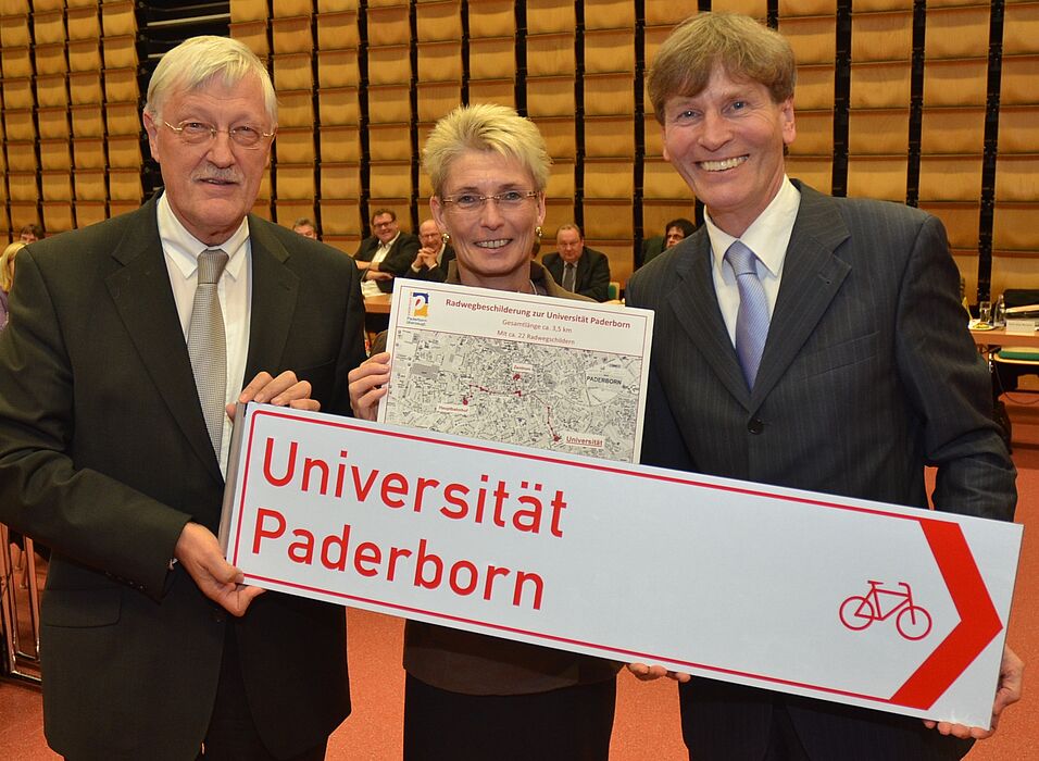Hier geht's zur Universität Paderborn. Bürgermeister Heinz Paus (r.) und Claudia Warnecke, Technische Beigeordnete der Stadt Paderborn, überreichten Prof. Dr. Nikolaus Risch, Präsident der Universität Paderborn, symbolisch dieses Schild.