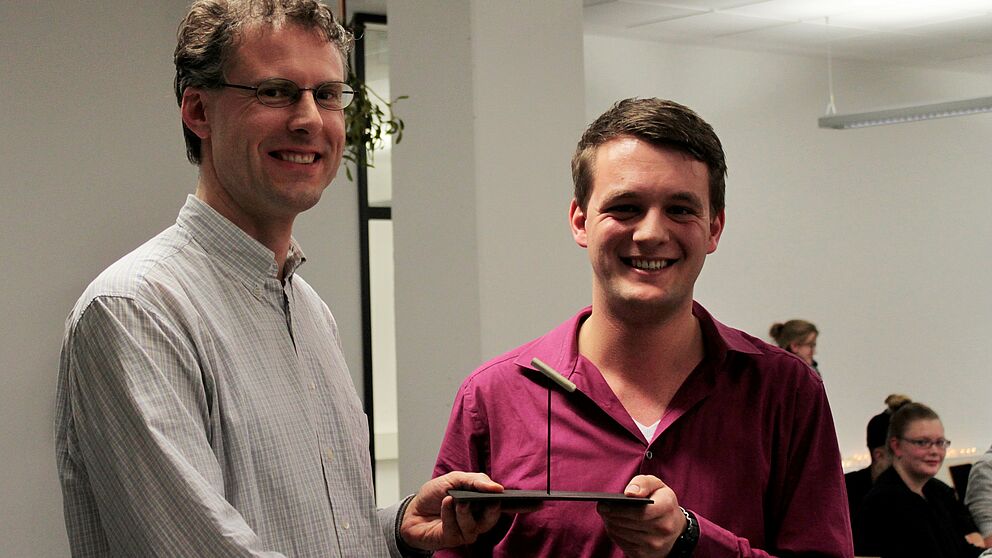 Foto (Department Physik): Prof. Dr. Arno Schindlmayr (li.) freut sich über die „Goldene Kreide“ für die beste Lehrveranstaltung, die ihm von Carsten Müller stellvertretend für die Fachschaft Physik überreicht wird.