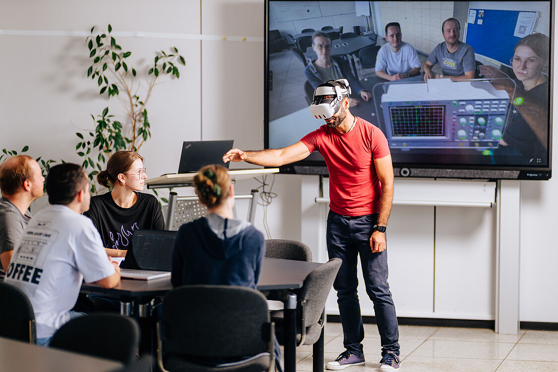 Studierender testet eine VR-Brille, weitere Studierende sehen auf einem Bildschirm, ein Messgerät, das der Studierende in der VR-Brille sieht