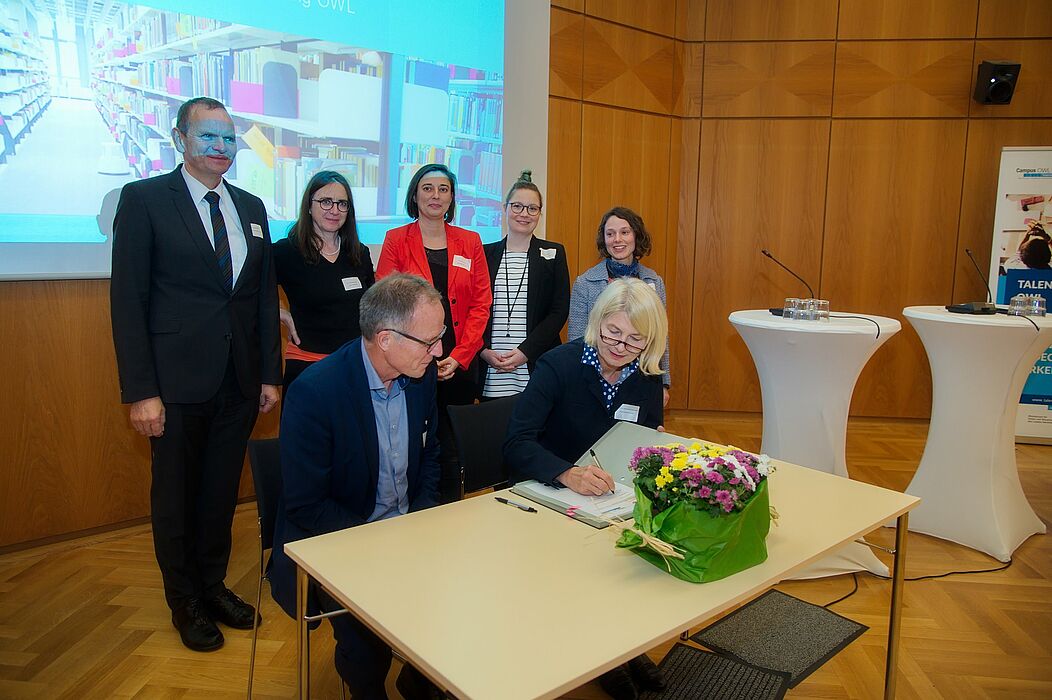 Foto (Arthur Isaak, Copyright: Hochschule OWL): Michael Uhlich (Bezirksregierung Detmold) (vorne li.) und Professorin Ingeborg Schramm-Wölk (Vorsitzende Campus OWL / Präsidentin der FH Bielefeld) unterzeichnen im Beisein der Vertreterinnen und Vertreter von Campus OWL und Talentscouting OWL eine Kooperationsvereinbarung, um damit die Zusammenarbeit mit den Schulen in der Region zu stärken.