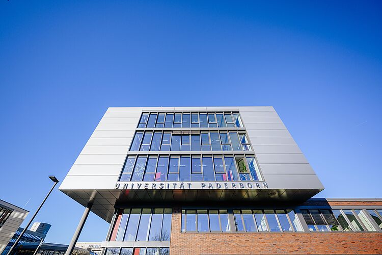 Das Q-Gebäude der Universität Paderborn erstreckt sich vor blauem Himmel mit seiner modernen Fensterfront in die Höhe.