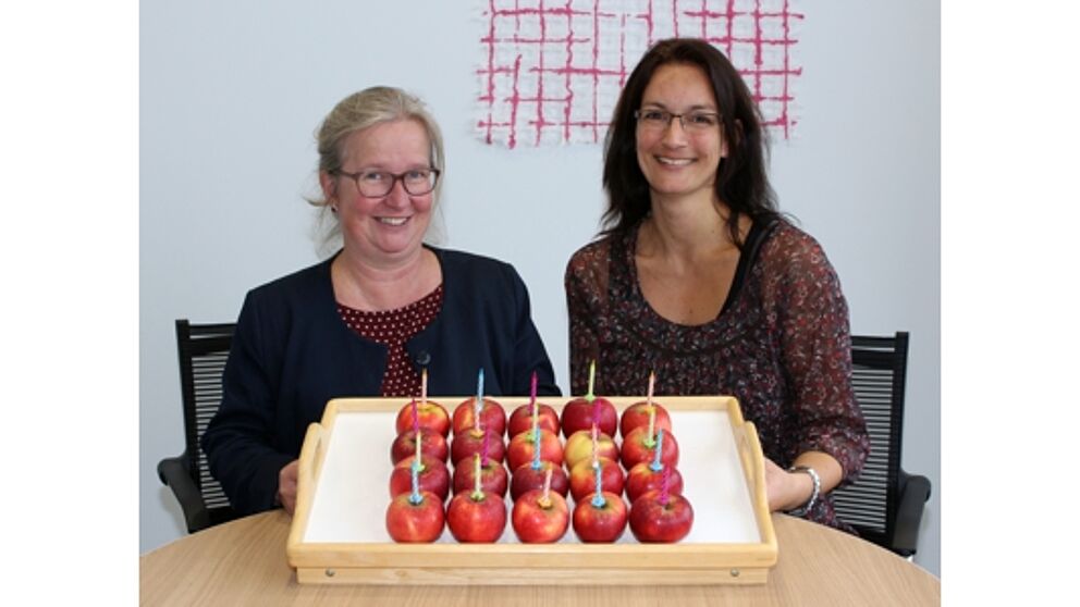 Foto (Universität Paderborn, Heiko Appelbaum): Simone Probst (links) und Sandra Bischof haben zum Jubiläum einen vitaminreichen Geburtstagskuchen vorbereitet.
