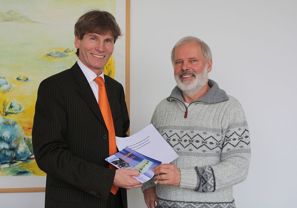 Foto (Universität Paderborn, Frauke Döll): Dr. Uwe Rheker (rechts) übergibt seinen letzten Bericht als Beauftragter für Behindertenfragen der Universität an Präsident Prof. Dr. Nikolaus Risch.
