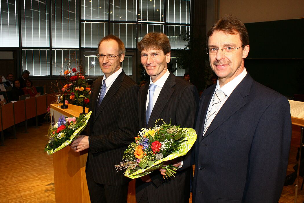 Foto (Mark Heinemann): NRW-Innovationspreisträger Prof. Dr. Reinhold Noé (li.) und Prof. Dr. Ulrich Rückert erhielten aus der Hand von Prof. Dr. Nikolaus Risch Blumen.