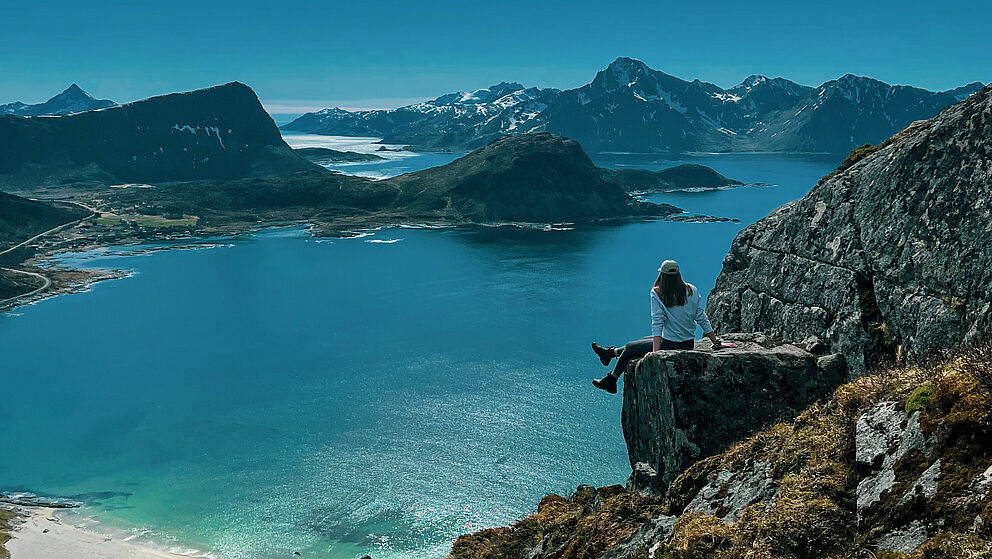Eine junge Frau sitzt auf einer Klippe über dem Meer in einer idyllischen Landschaft.