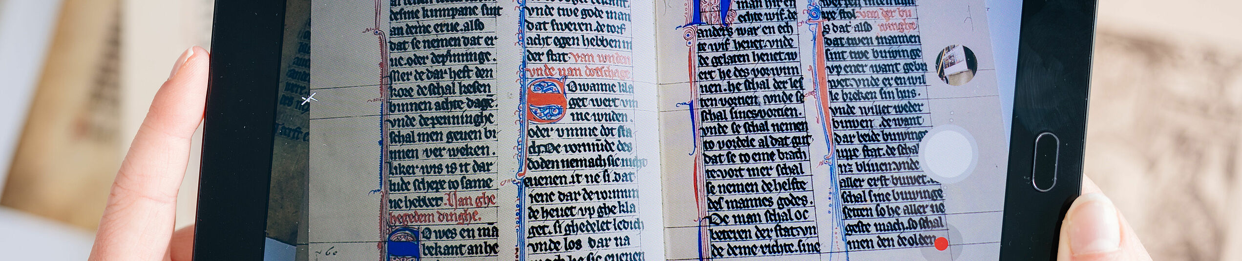 A book with medieval script is displayed on a tablet held in both hands