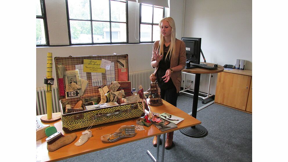 Abbildung: Erika Schrainer vor ihrem Museumskoffer mit dem Titel“ Tempel der Arbeit“.