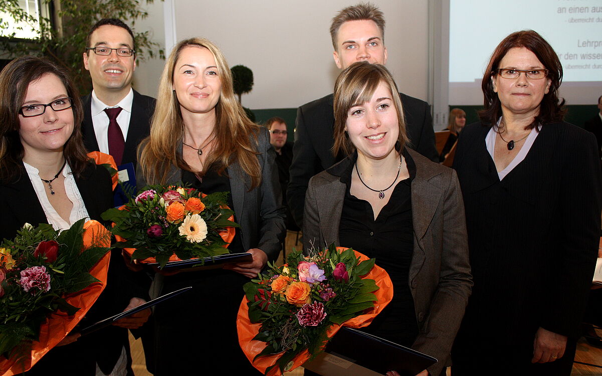 Die fünf Lehrpreisträger:innen stehen neben der Vizepräsidentin vorne im Hörsaal und halten Blumensträuße in der Hand. 