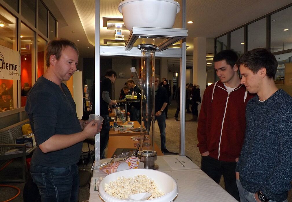Foto (Universität Paderborn, Jasmin Rostam): Steffen Franke (li.) gibt Einblick in das Fach Chemie und zeigt Schülern, wie Popcorn hergestellt wird.