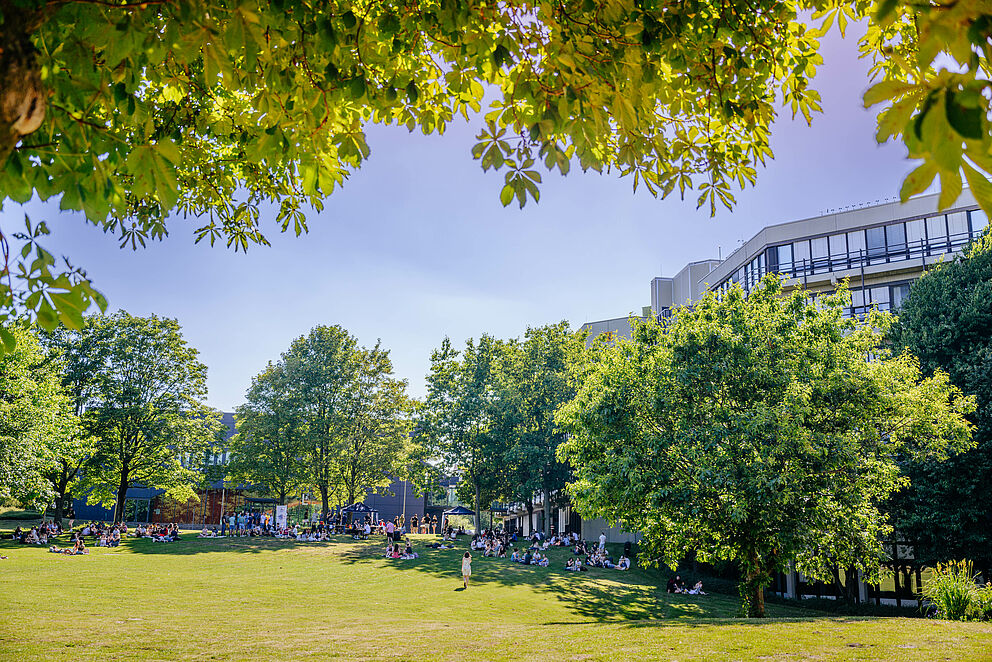 Auf der grünen Wiese hinter dem Audimax der Universität Paderborn sammeln sich Studierende.