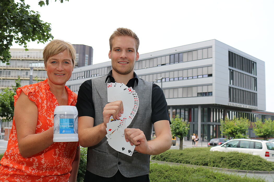 Foto (Universität Paderborn, Juliane Fröhling): Alexandra Dickhoff von Alumni Paderborn und Zauberer David Wedegärtner mit Kartentricks und Alumni-Krug beim kommenden Ehemaligen-Treffen der Universität.