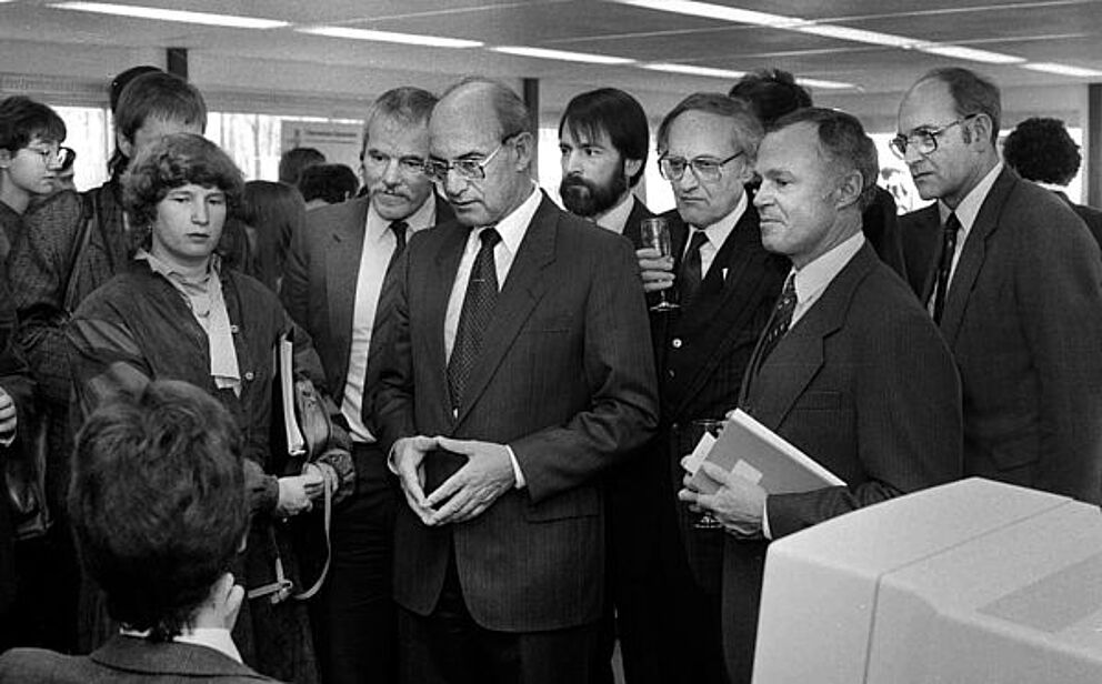 Schwarz-weiß Foto, mehrere Personen stehen versammelt vor einem Computer und schauen diesen an.