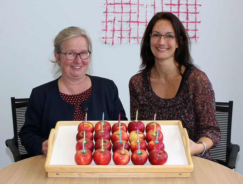 Foto (Universität Paderborn, Heiko Appelbaum): Simone Probst (links) und Sandra Bischof haben zum Jubiläum einen vitaminreichen Geburtstagskuchen vorbereitet.