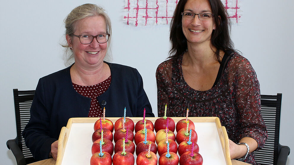 Foto (Universität Paderborn, Heiko Appelbaum): Simone Probst (links) und Sandra Bischof haben zum Jubiläum einen vitaminreichen Geburtstagskuchen vorbereitet.