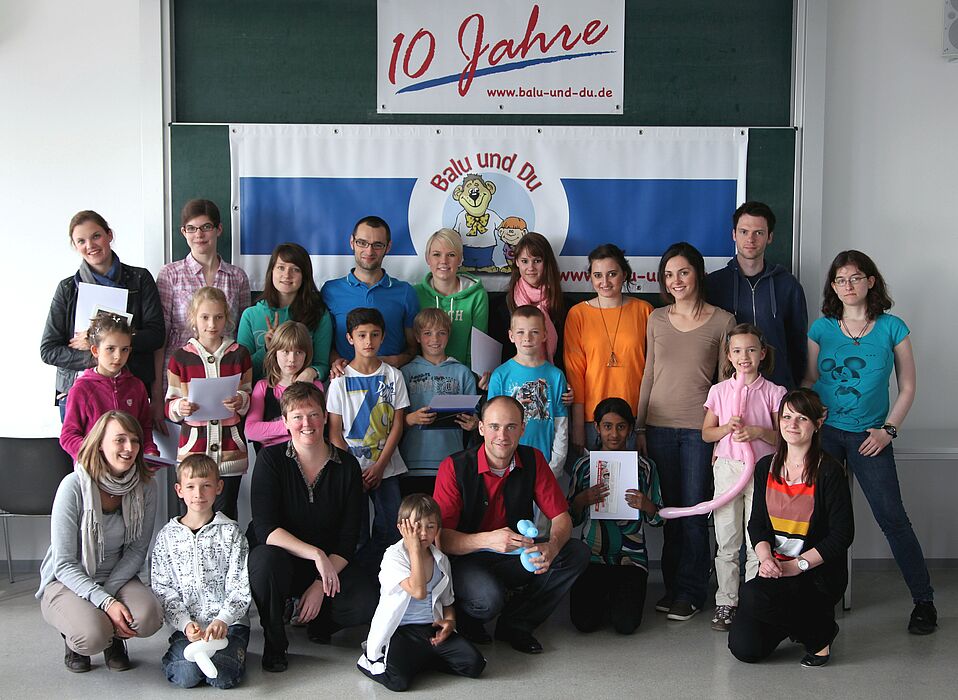 Foto: Projektkoordinatorin Sarah Rölker (vordere Reihe, 3. von links), Zauberer Jean Olivier (5. von links) und die Moglis mit ihren Balus bei der 10 Jahr-Feier des Projekts "Balu und Du".
