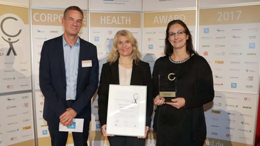 Foto (EuPD Research Sustainable Management GmbH): (v. l.) Thomas Holm, Leiter des Gesundheitsmanagements bei der Techniker Krankenkasse, überreichte den Preis an Diana Riedel und Sandra Bischof.