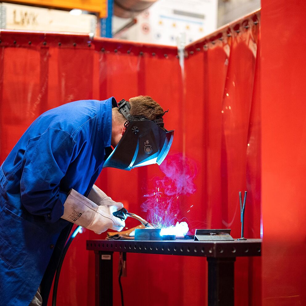 Ein Student mit Schutzkleidung beim Schweißen in der Werkstatt