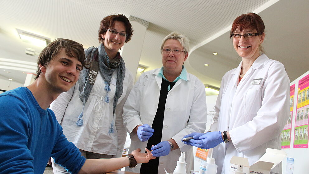 Foto (Universität Paderborn, Heiko Appelbaum): Auch der Student Till Tolckmitt ließ seine Blutzuckerwerte ermitteln. Das Angebot der Arzthelferinnen Elke Pätzold und Christel Lücke (v. r.) vom Betriebsärztlichen Dienst Bethel stieß auf großes Inter